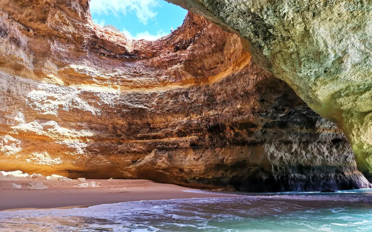 A catamaran on flat turquoise water beside the Algarve cliffs