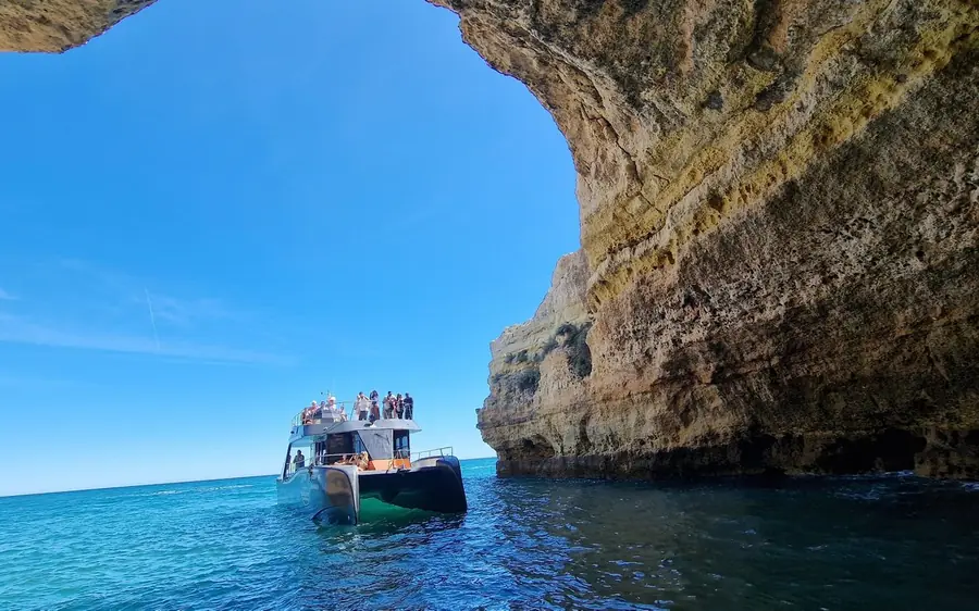 A catamaran on flat turquoise water beside the Algarve cliffs
