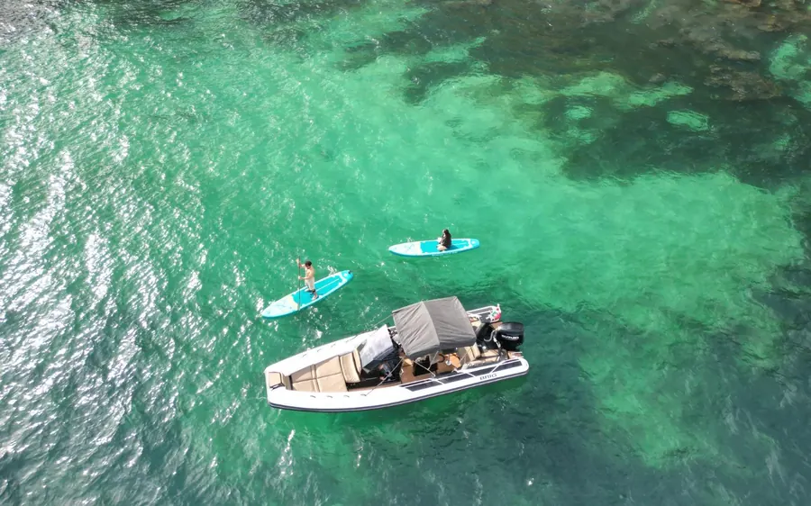 A charter boat on turquoise water with two paddleboards alongside